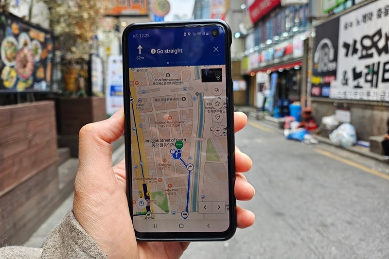 A traveler holds a phone running Naver Map on a Korean street while navigating in Seoul.