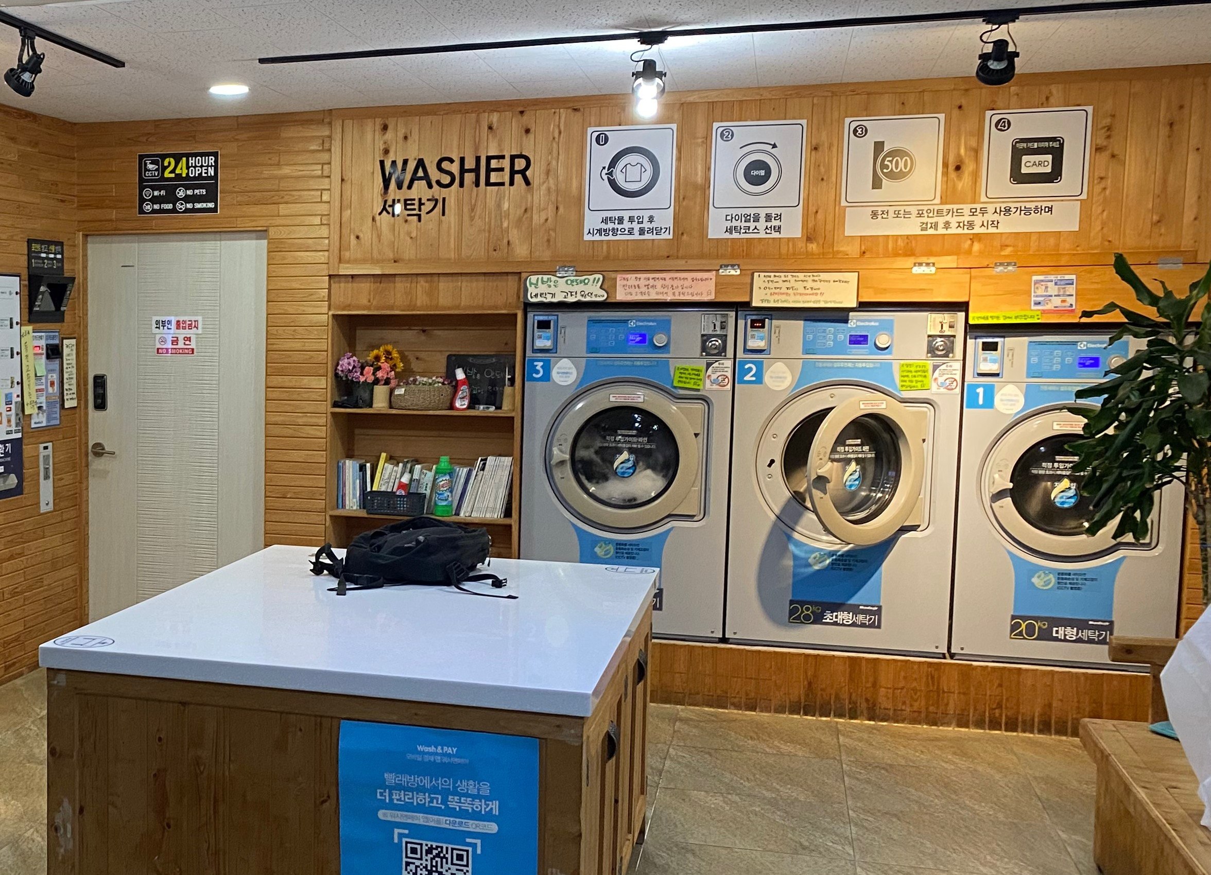 Korean self-service washing machines with washer signage, numbered machines, a folding table, and payment instructions.
