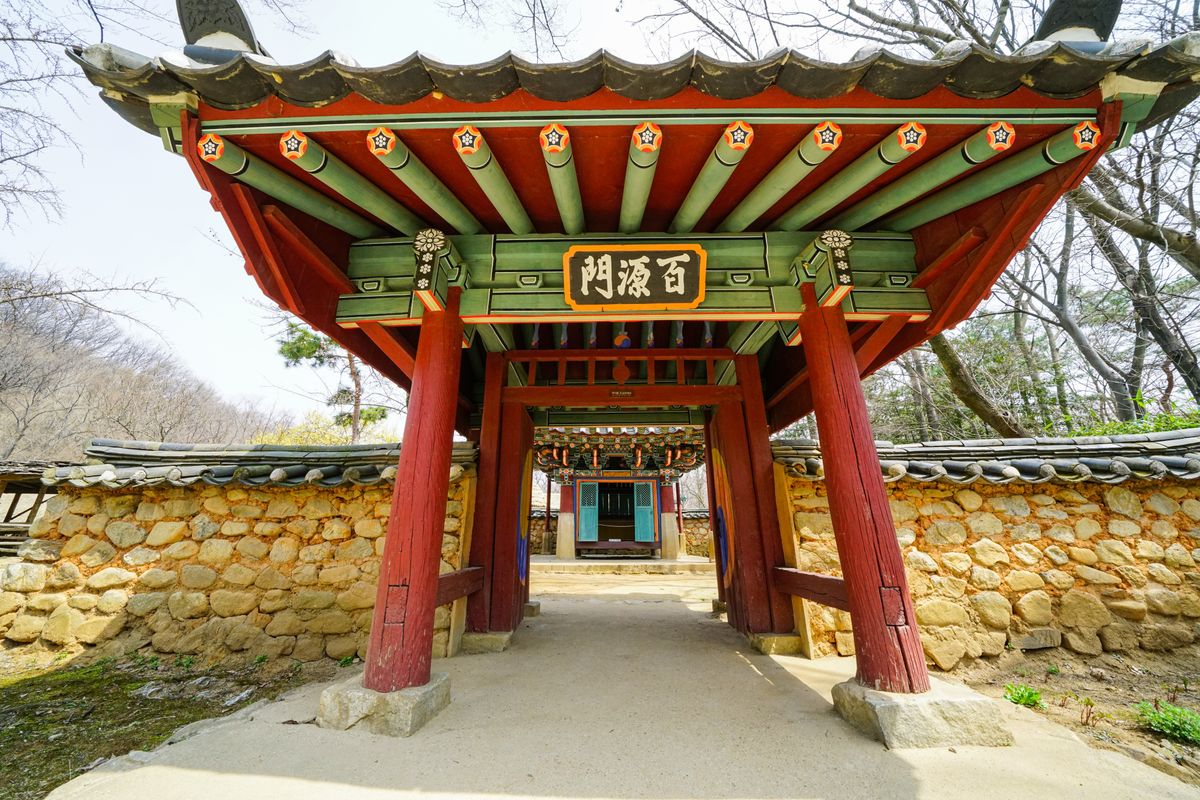 A vivid Korean temple gate framed by trees and stone walls.