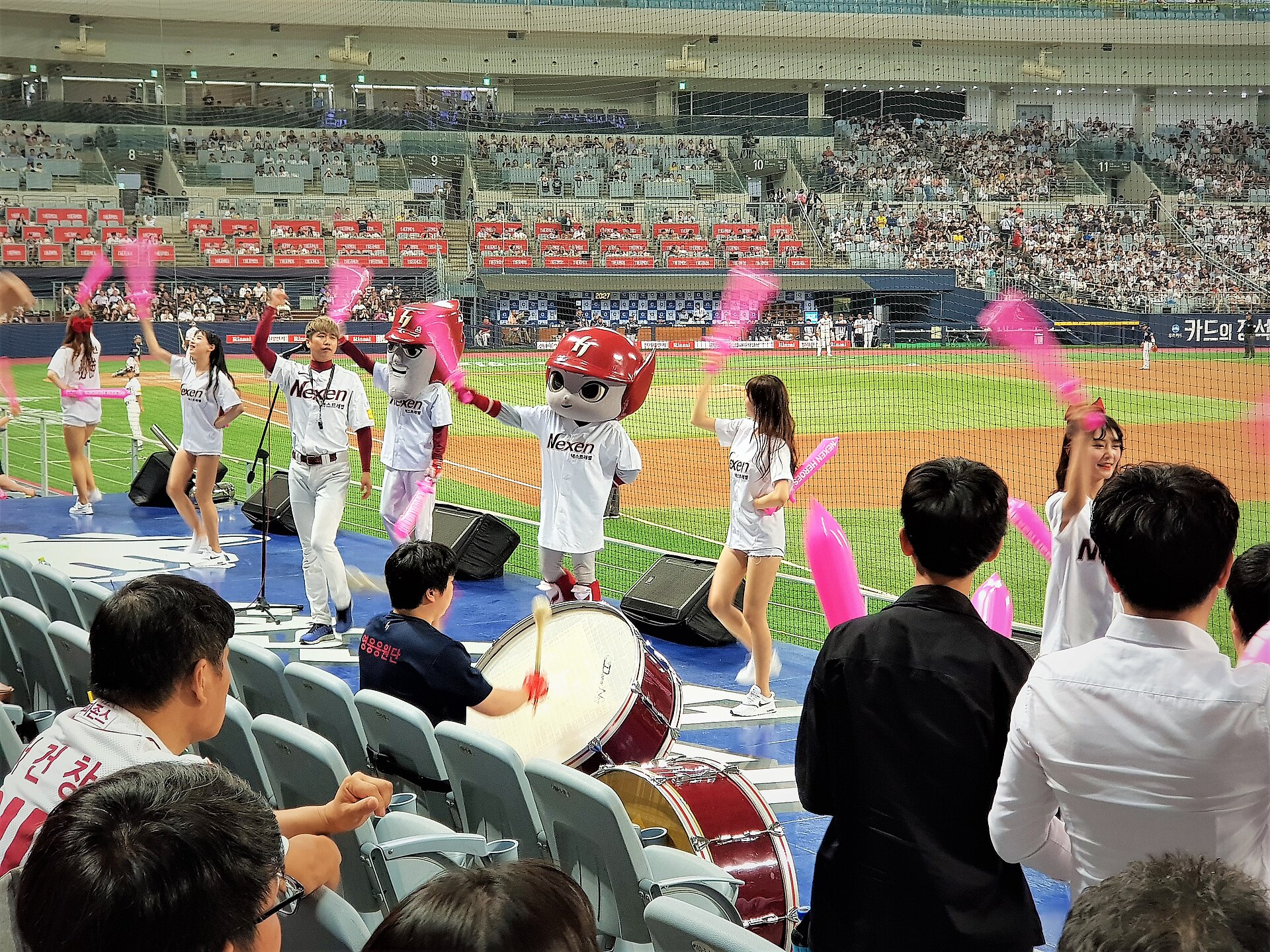 Kiwoom Heroes cheering stage at Gocheok Sky Dome with fans, mascot, drums, and pink clappers.