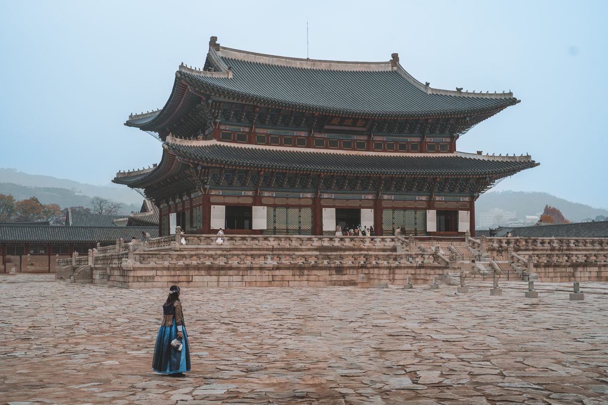 A visitor in hanbok standing in front of a large palace hall at Gyeongbokgung.