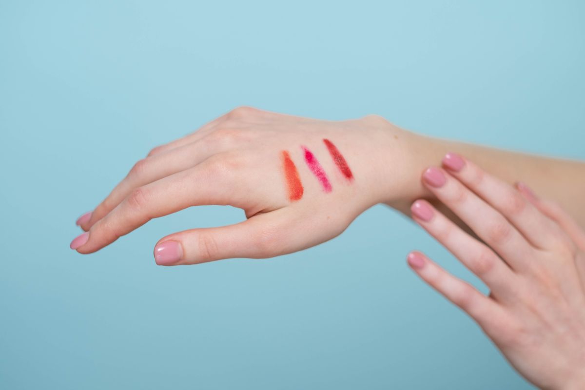 Lipstick swatches on a hand against a soft blue background.