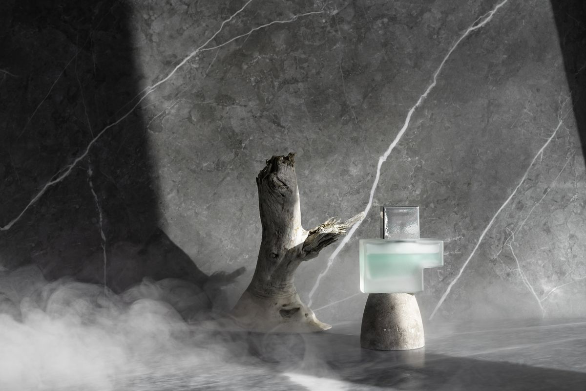 A minimal perfume bottle displayed with smoke and stone textures.
