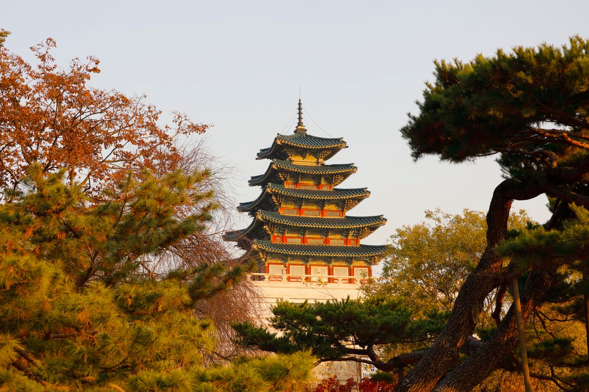 Gyeongbokgung Palace pagoda framed by autumn leaves in Seoul.