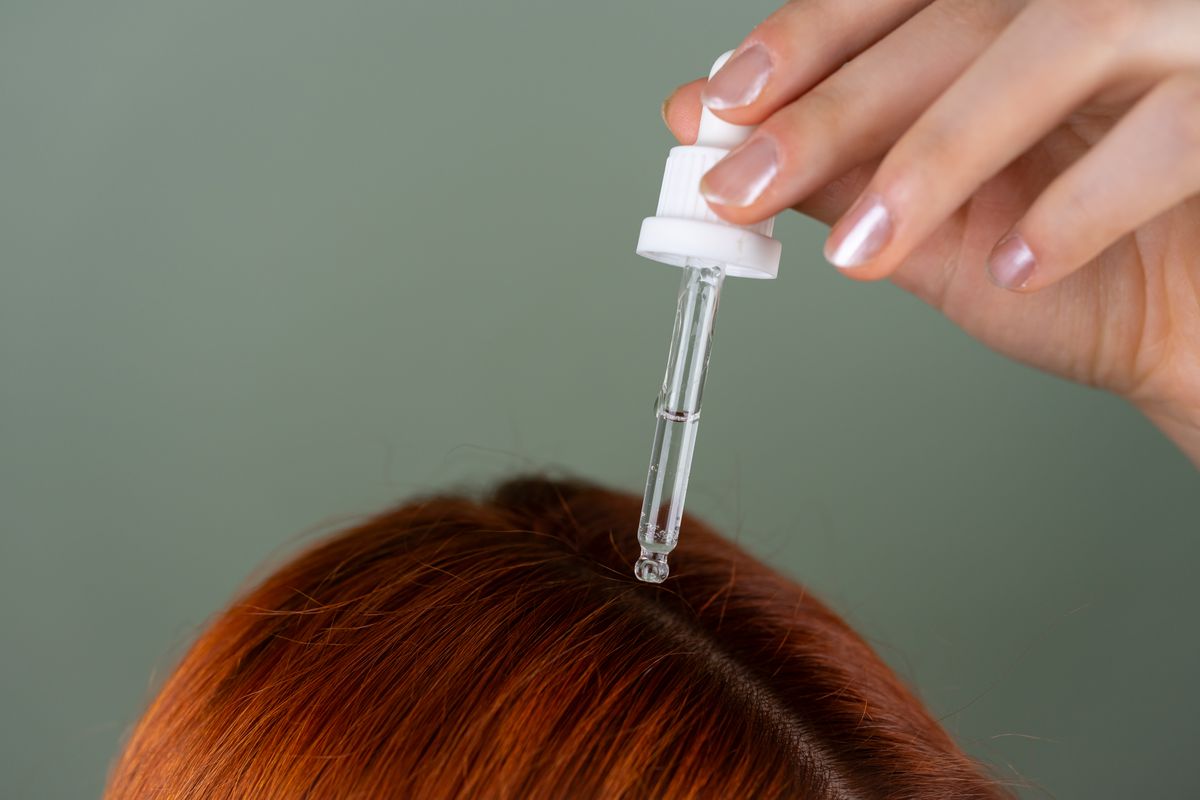 A dropper applying clear scalp serum near the hair roots.