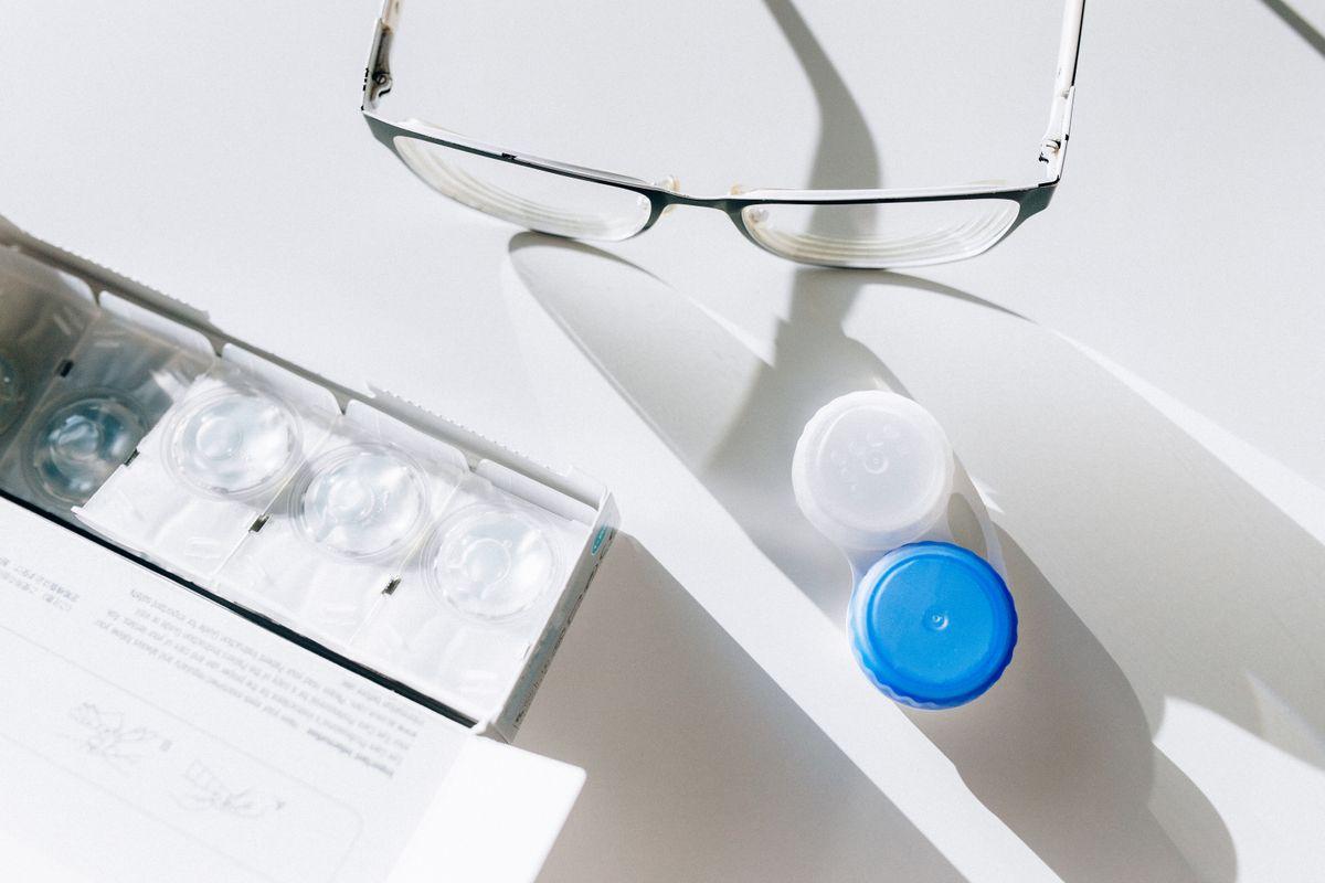 A contact lens case, contact lens packs, and eyeglasses on a white surface.