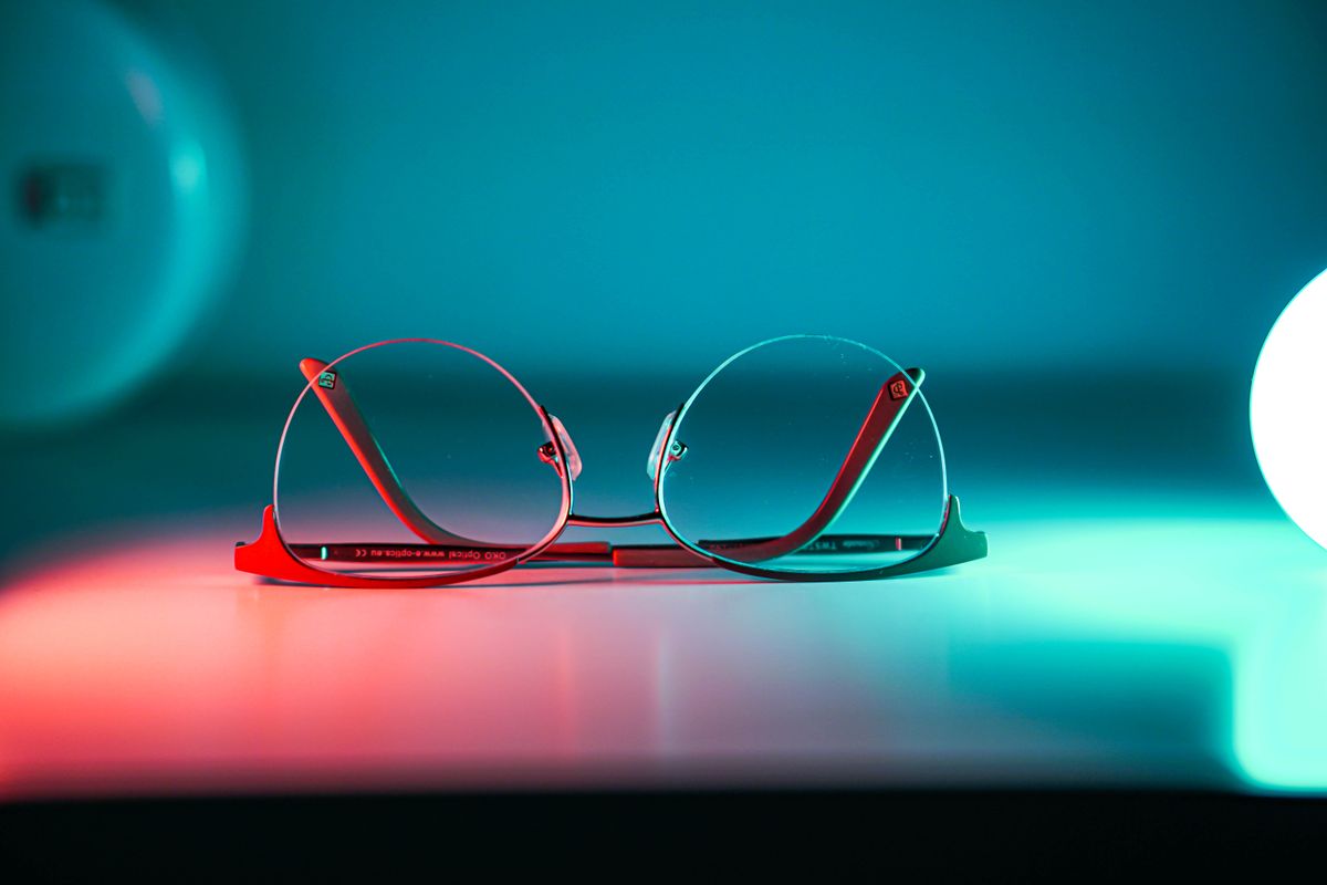 A pair of eyeglasses lit by colorful neon light.