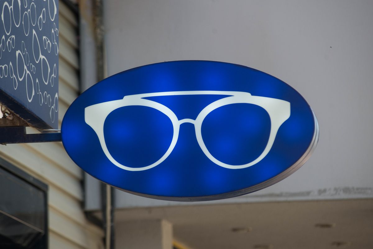 A blue illuminated sign with an eyeglasses icon outside an eyewear store.