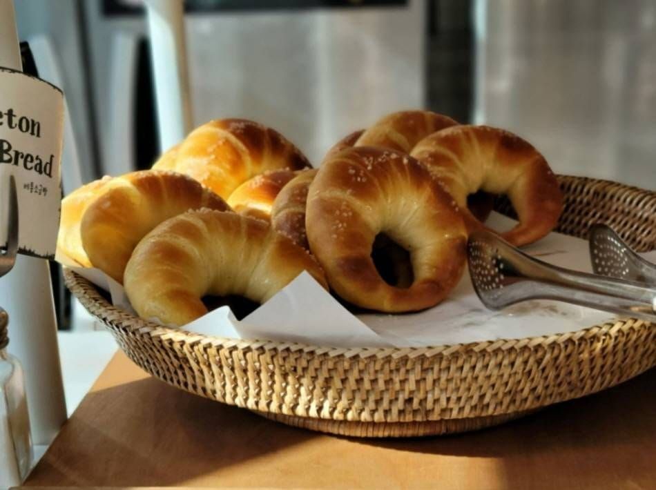 Salt bread rolls piled in a woven basket at the Beton counter, with serving tongs and a small sign reading Beton Salt Bread.