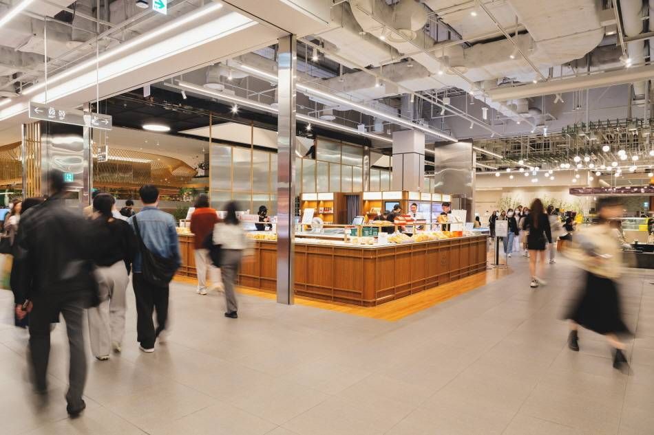 A busy indoor food counter area at The Hyundai Seoul's Tasty Seoul food hall, with shoppers moving through prepared-food counters.