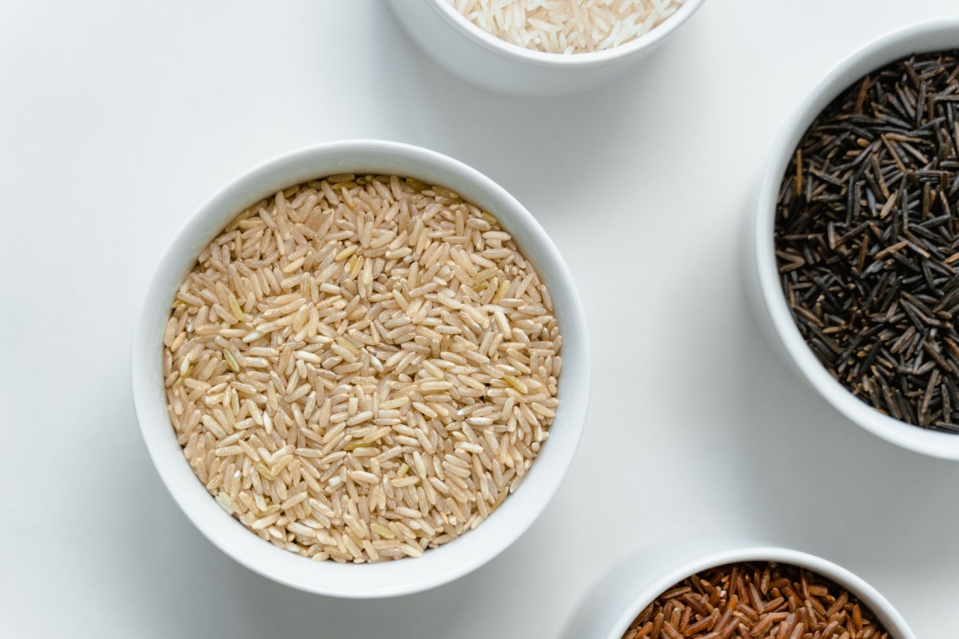 Bowls of different rice and grains arranged on a clean surface.