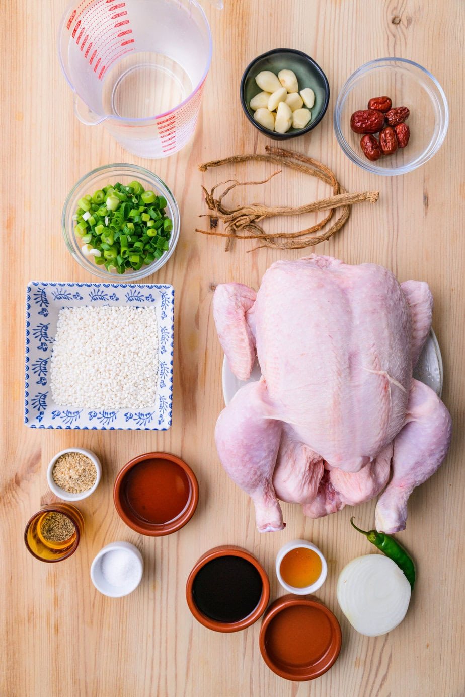 Samgyetang ingredients laid out with a whole chicken, ginseng, garlic, jujubes, rice, and green onion.