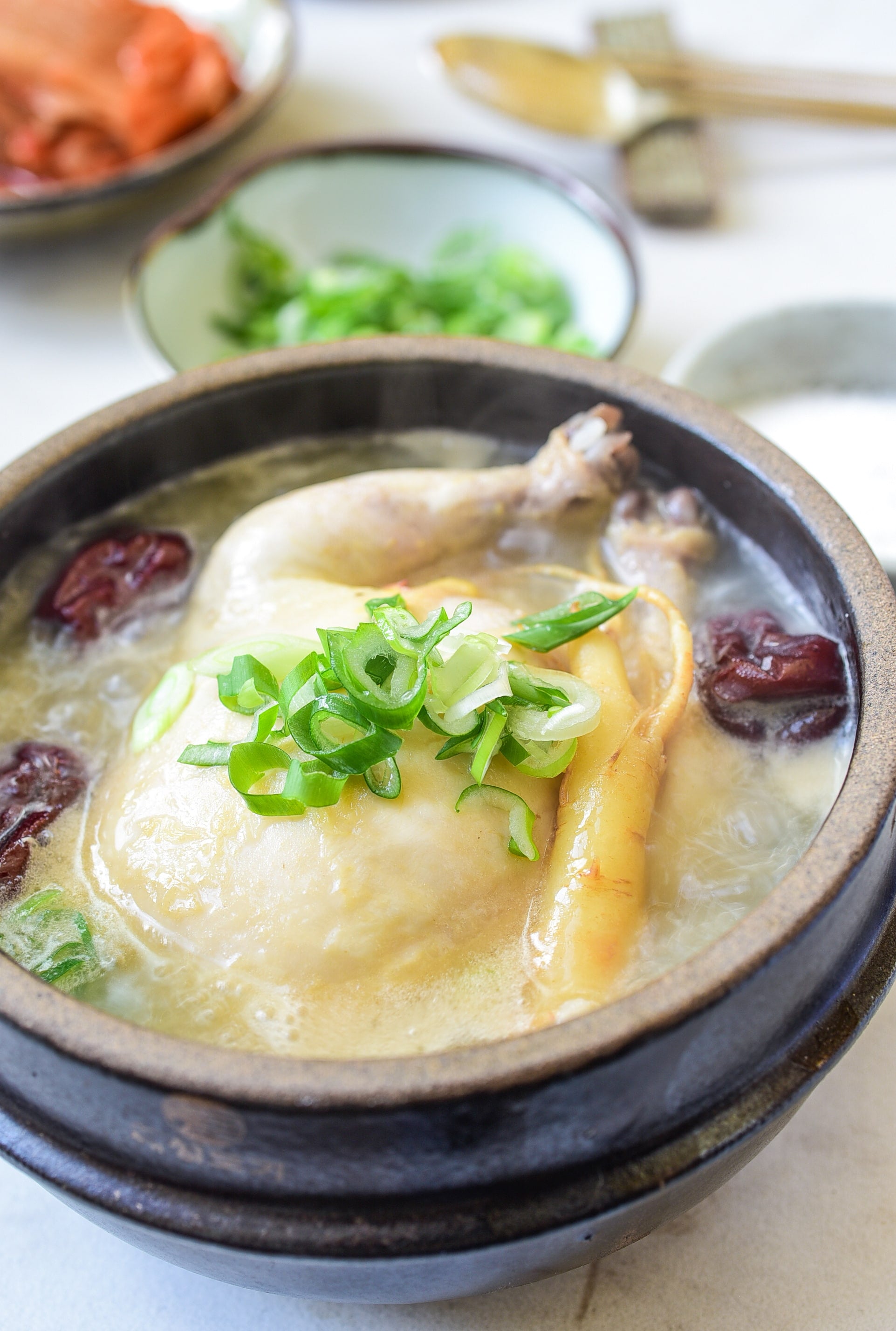 A steaming samgyetang bowl with ginseng, scallions, and a whole chicken in broth.