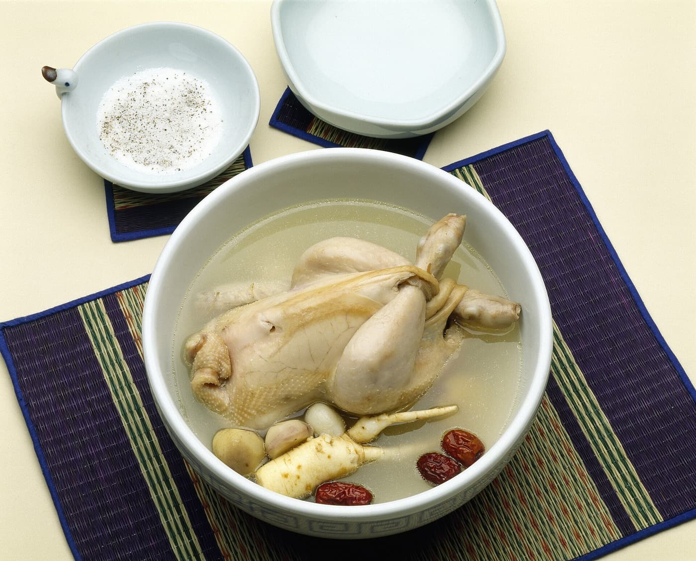 A whole young chicken in a stone bowl of clear samgyetang broth.