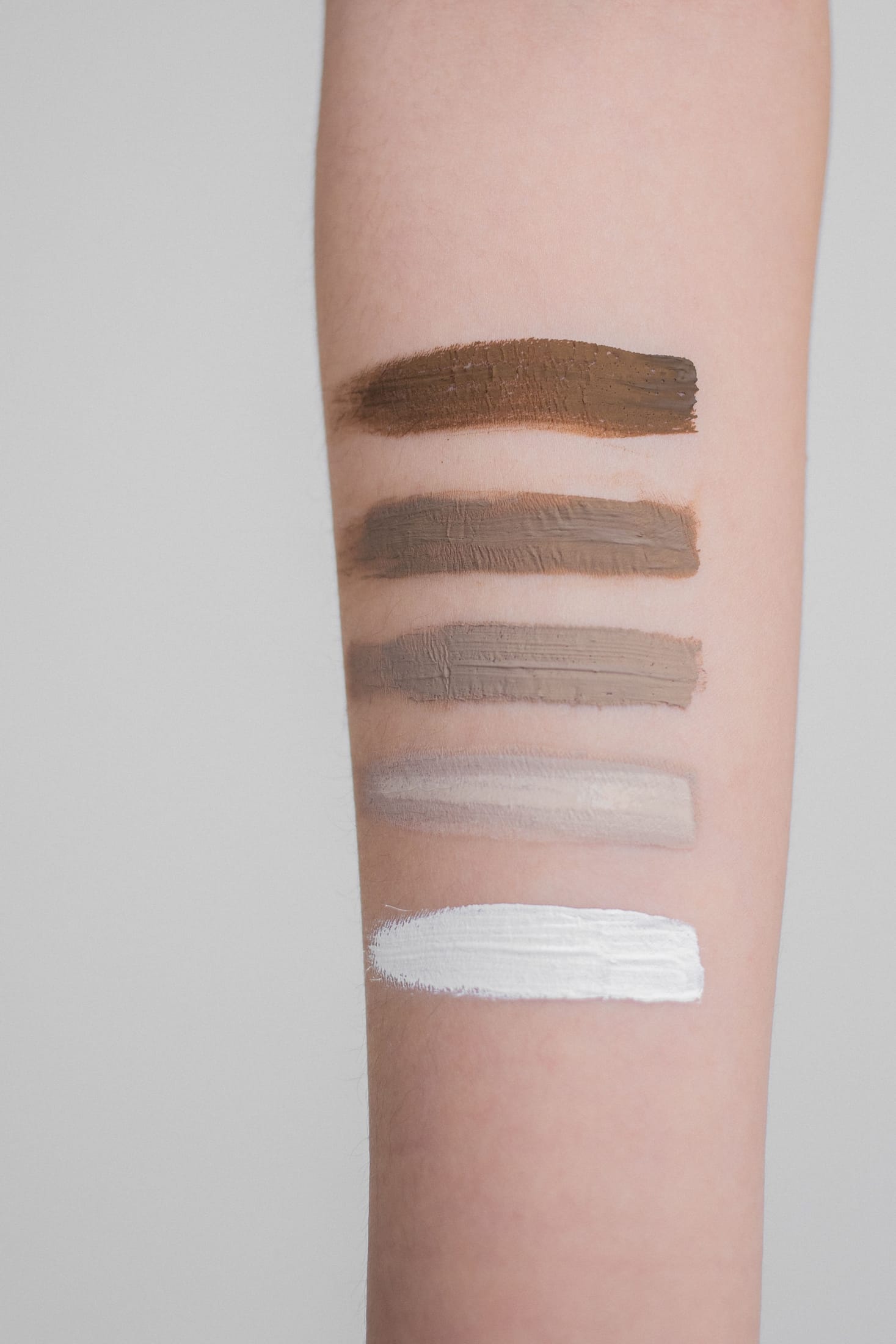 Five foundation shade swatches tested on a forearm, from deep to light, to compare undertones.