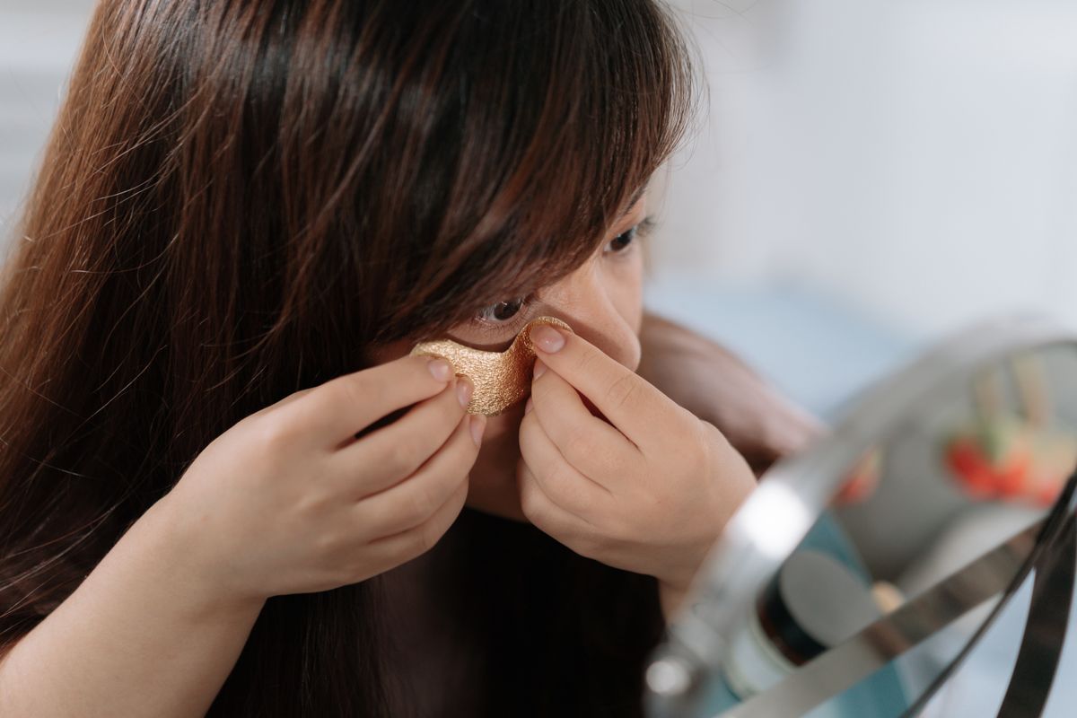 A woman applies under-eye patches as part of a skincare routine.