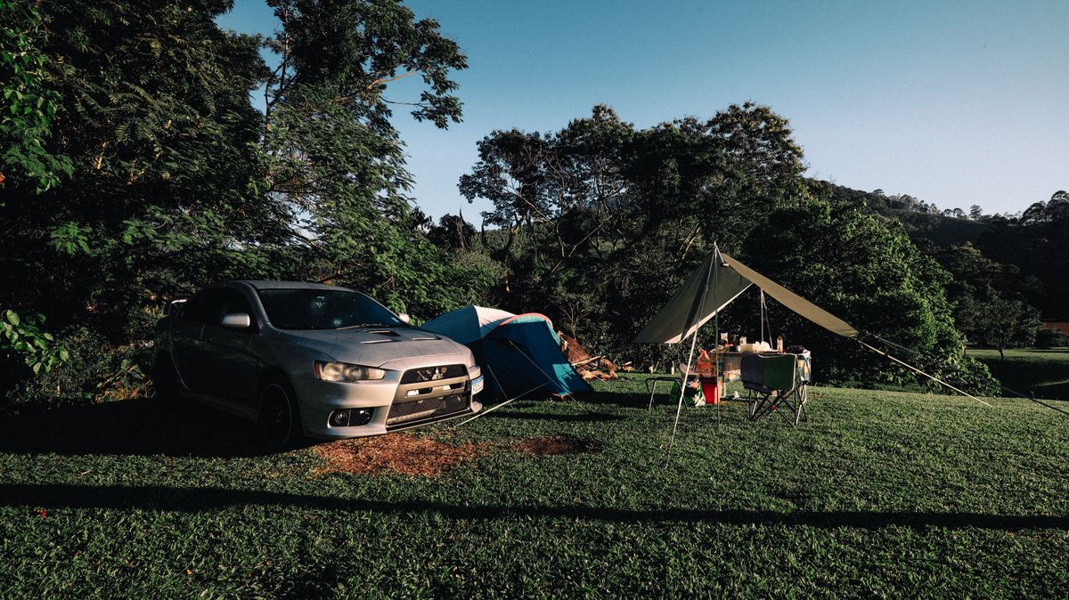 A parked car and tent set up in a green campsite, showing the kind of weekend gear layout car campers plan around.