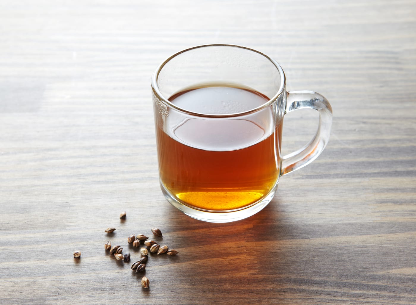 A clear cup of Korean boricha barley tea with roasted barley grains on the table.