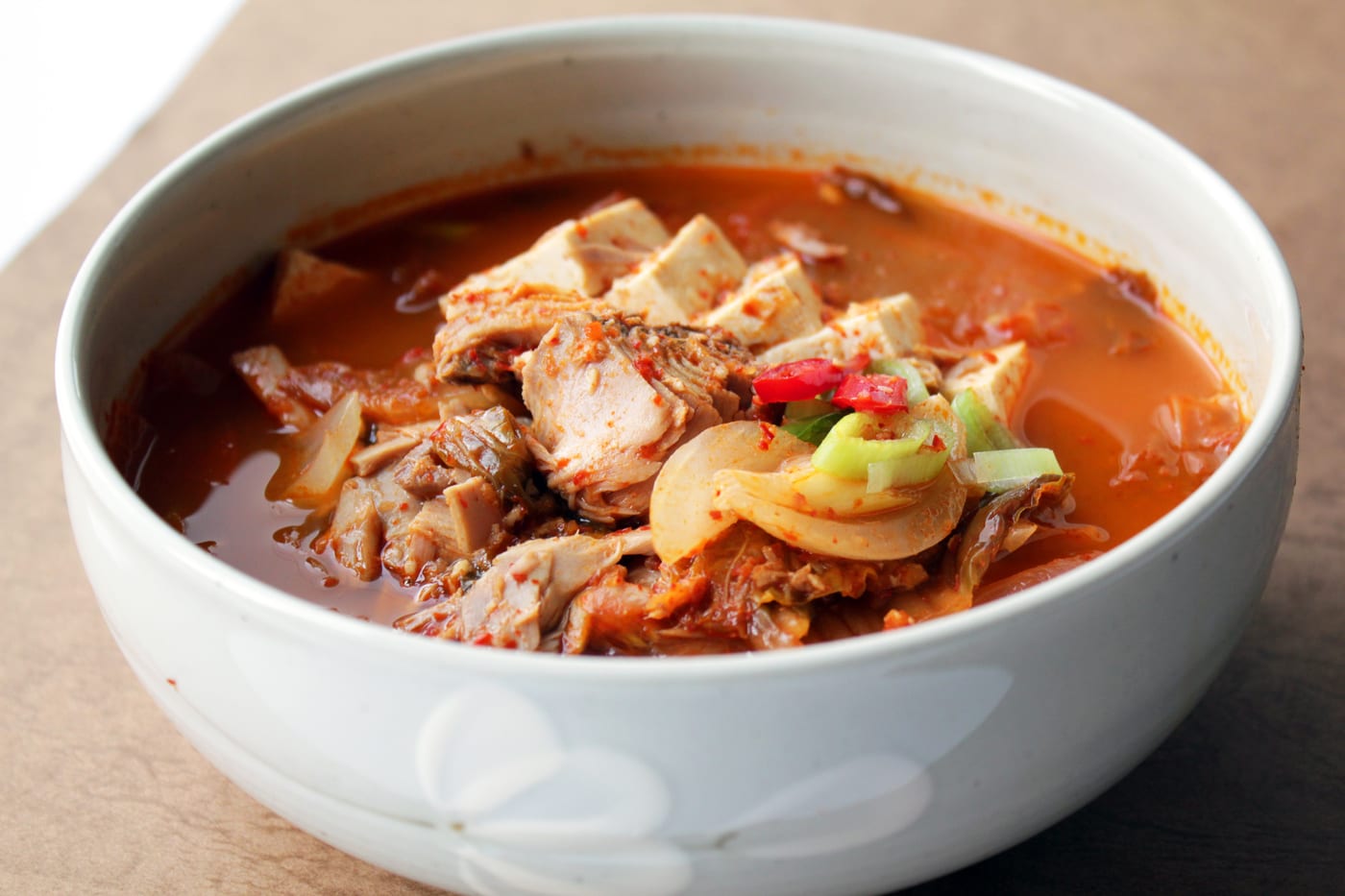 A bowl of tuna kimchi jjigae with tofu and red broth.