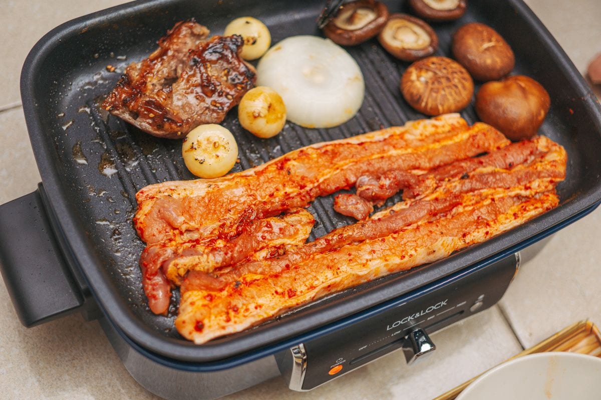 Pork belly, mushrooms and onions cooking in separate zones on an electric grill