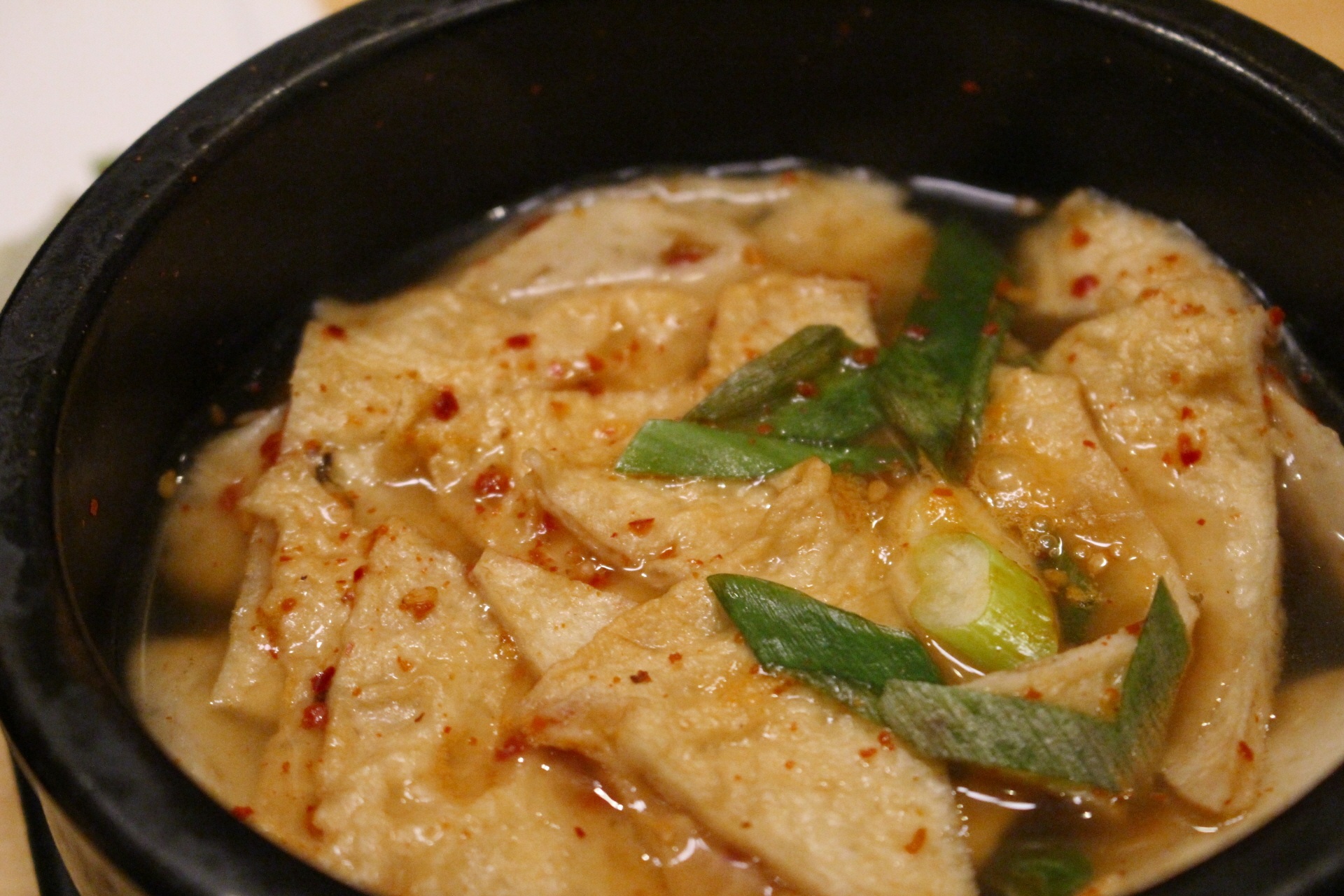A black bowl filled with Korean eomuk-tang, fish cakes in a hot lightly spicy broth.