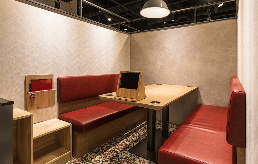 A private Red Button sofa booth with a table tablet, cup holders, and bench seating.