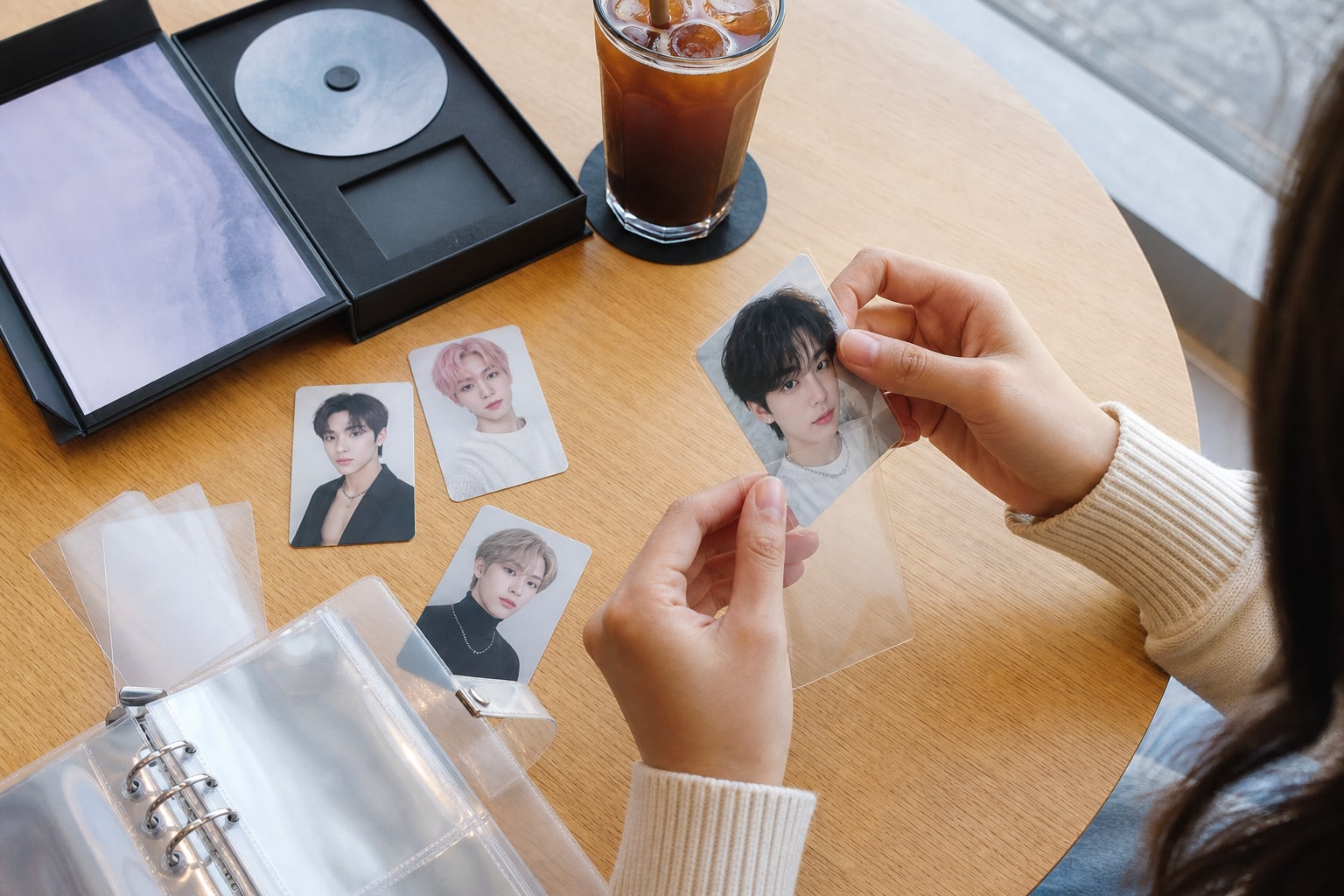 A collector sleeves a fictional K-pop photocard beside an opened album and binder.