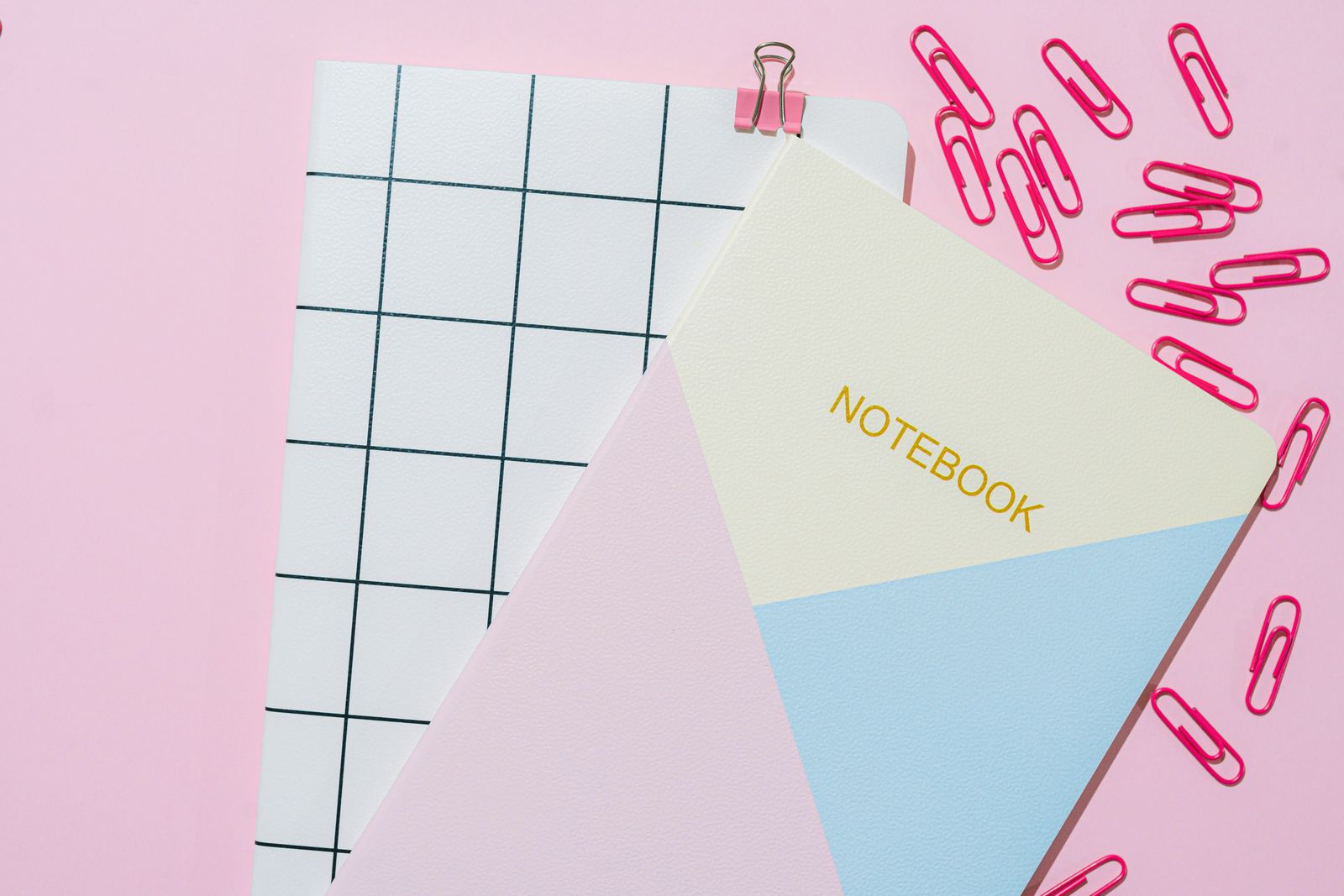Pastel notebooks and pink paper clips arranged on a desk.