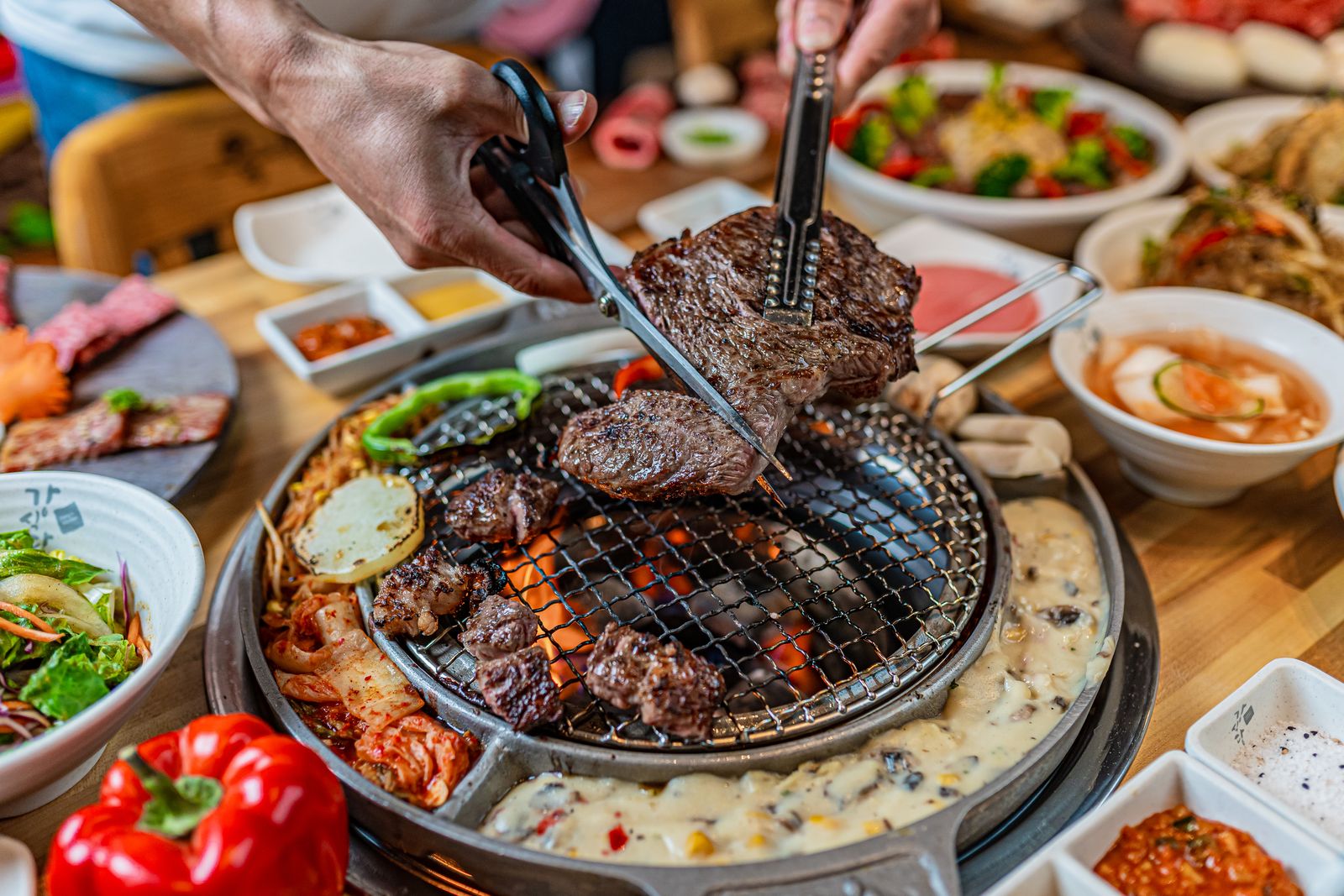 A diner cutting grilled beef with kitchen scissors while holding it with tongs.