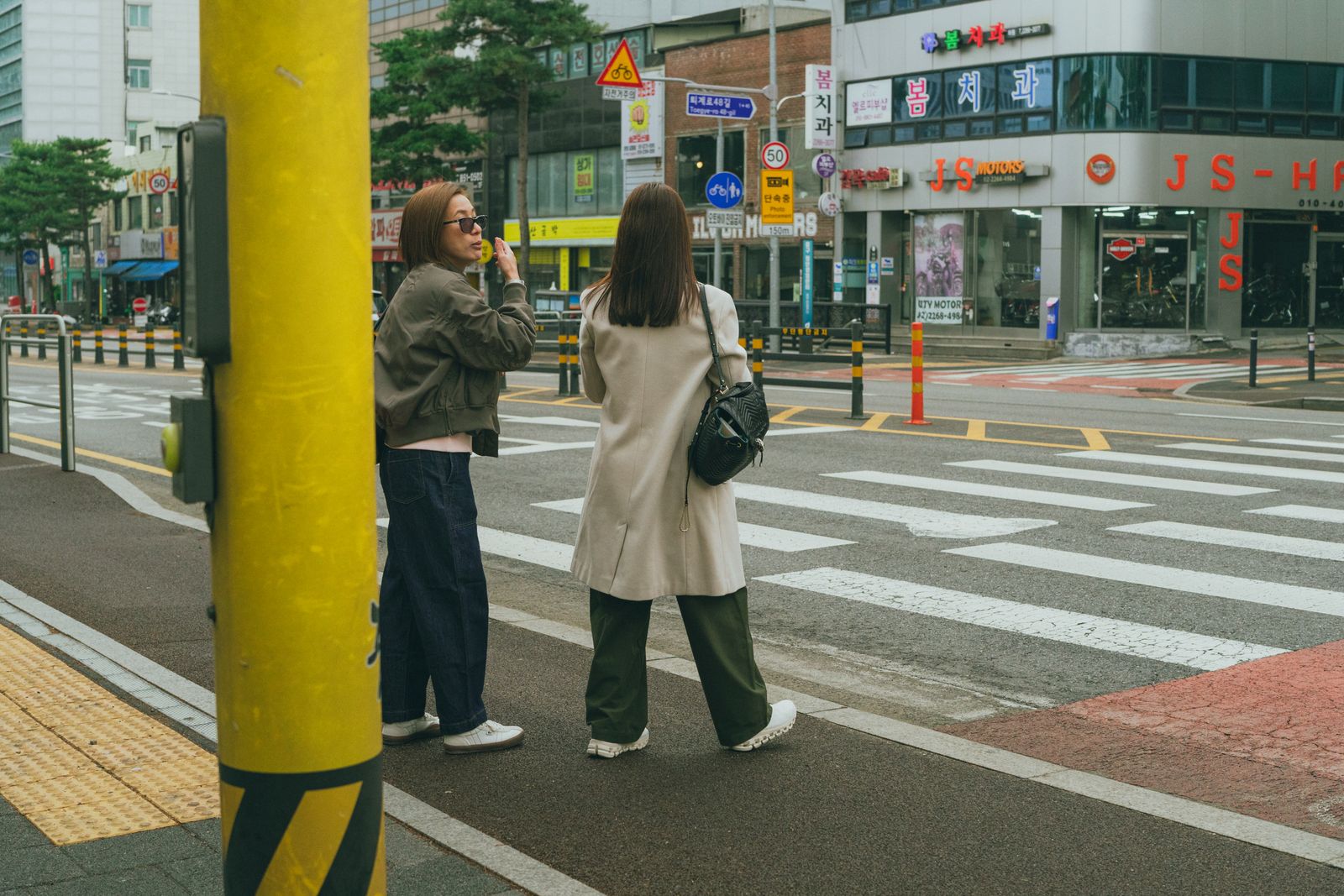Two women waiting at a crosswalk on a clearly Korean street.