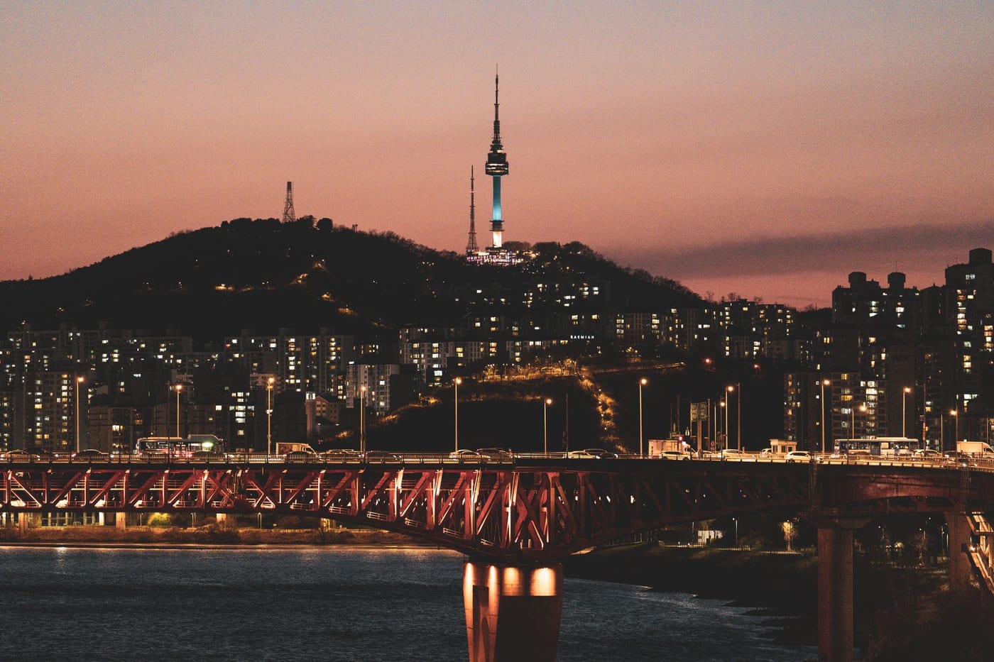 Seoul's evening skyline with N Seoul Tower lit up on Namsan and a bridge over the Han River.