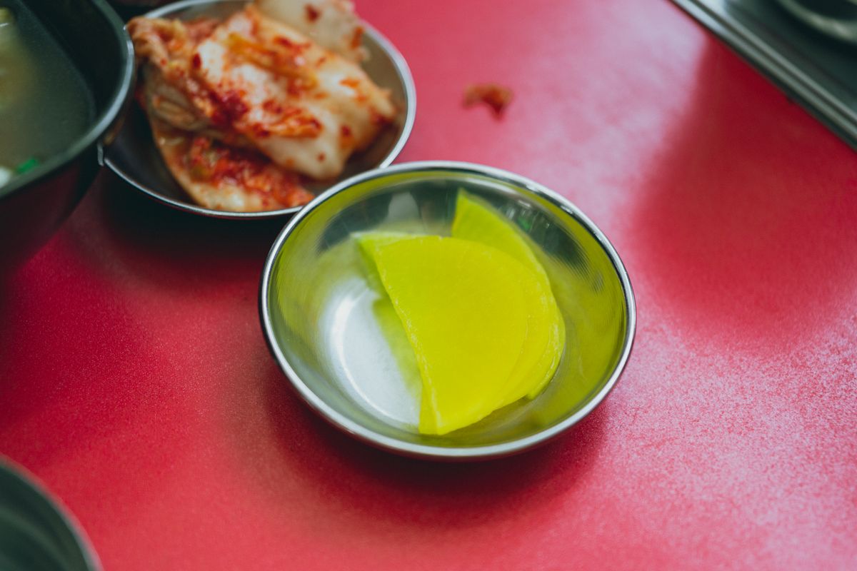 Kimchi and pickled radish banchan served in traditional Korean metal side-dish bowls.