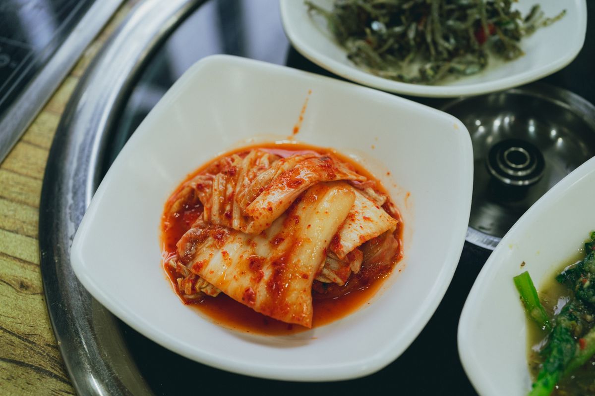 Close-up of traditional Korean kimchi served in a white bowl on a Korean metal dining tray.