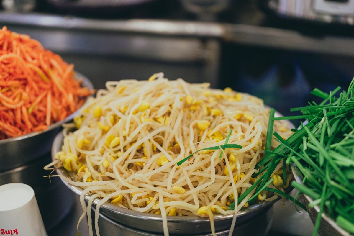 Fresh bean sprouts, shredded carrot, and chives at a Korean market, common banchan and kimchi ingredients.