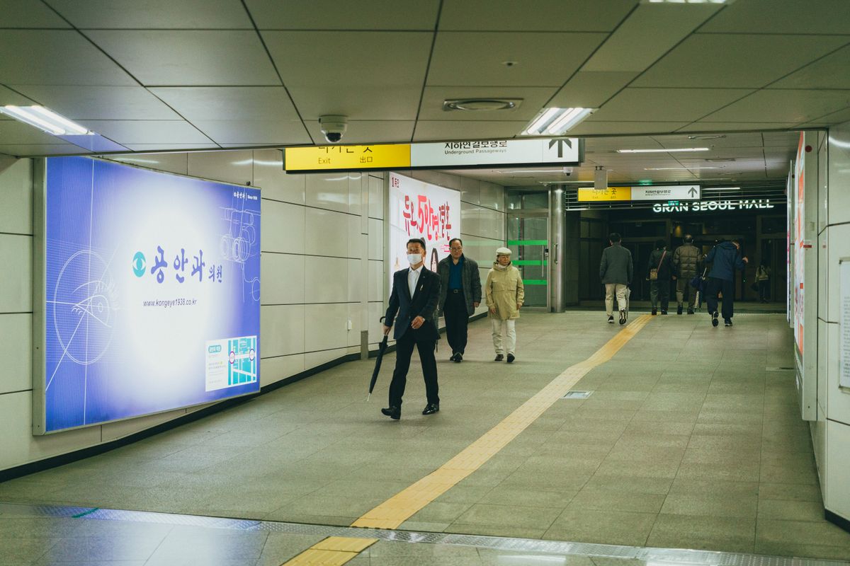 A Seoul subway passage with a large illuminated clinic advertisement beside commuters.