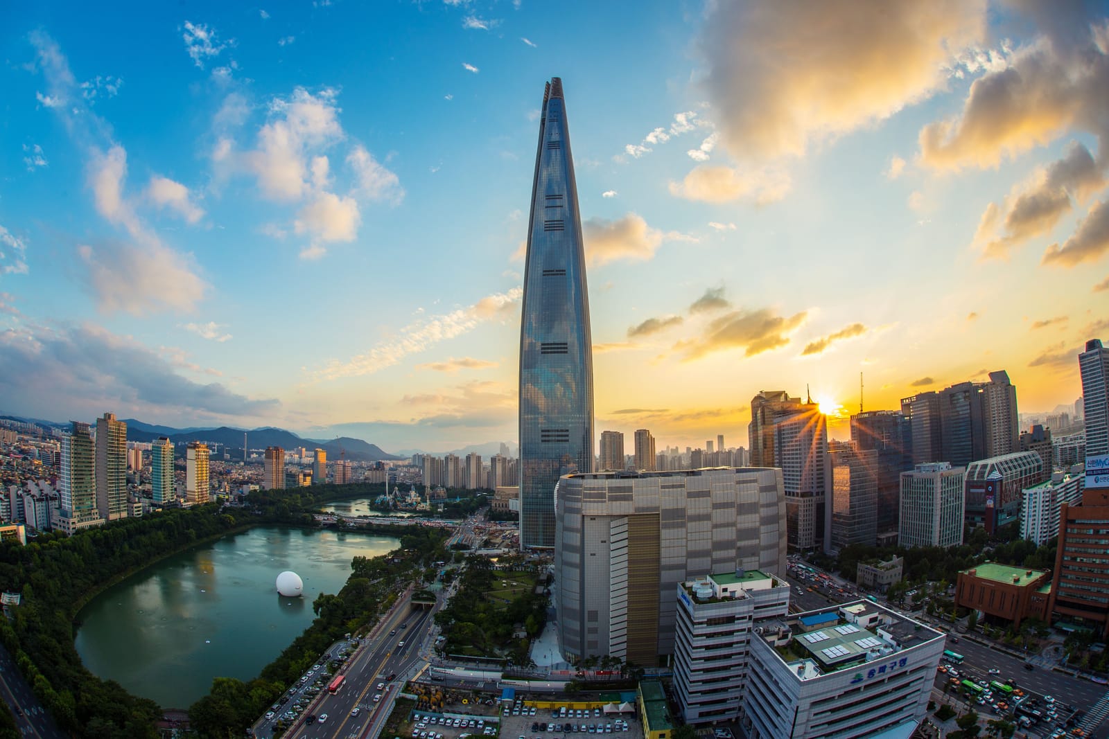 Lotte World Tower rising above Seokchon Lake and the Lotte World amusement park at sunset in Seoul.