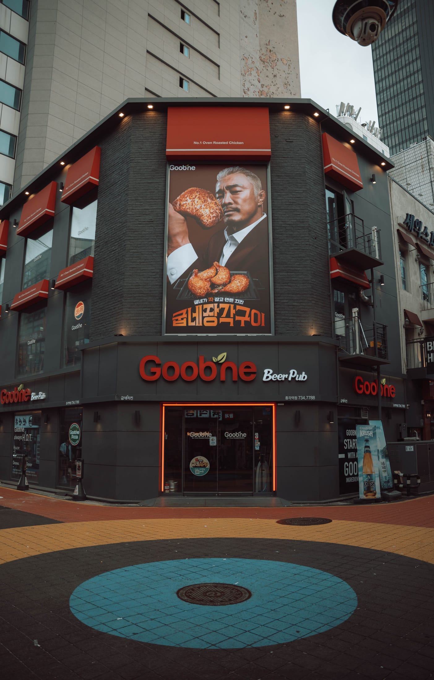 A Goobne Chicken storefront in South Korea with red-and-black branding and a large menu poster.