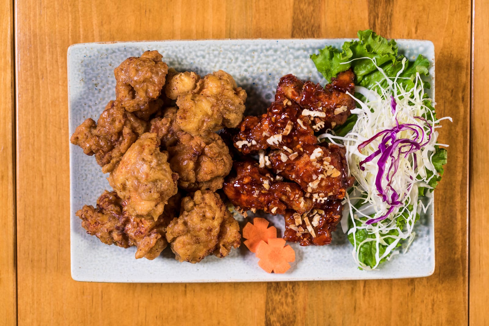 Half-fried, half-glazed Korean fried chicken plated with shredded cabbage, lettuce, and carrot garnish.