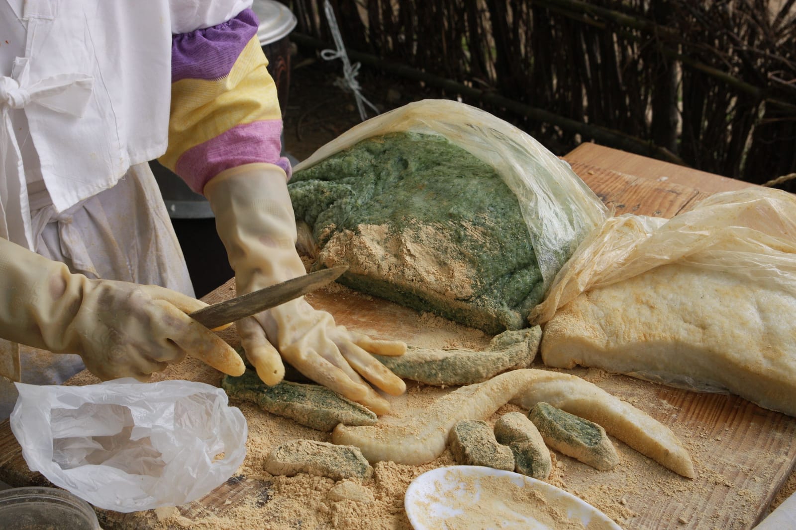 A worker in gloves cutting freshly made Korean rice cake dusted with bean powder on a wooden board.