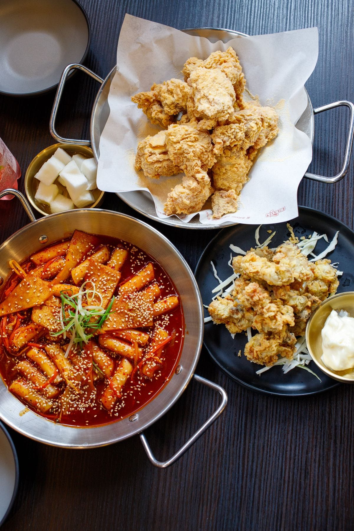 Korean fried chicken next to a pot of tteokbokki rice cakes in red sauce.