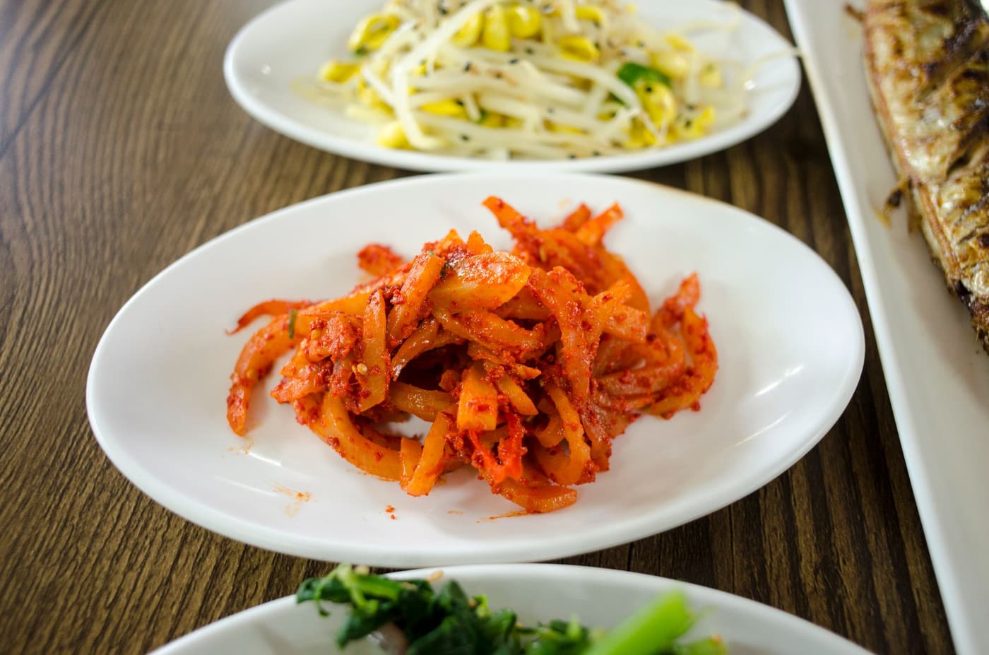 A spread of Korean side dishes including kimchi, greens and pickles in small bowls.