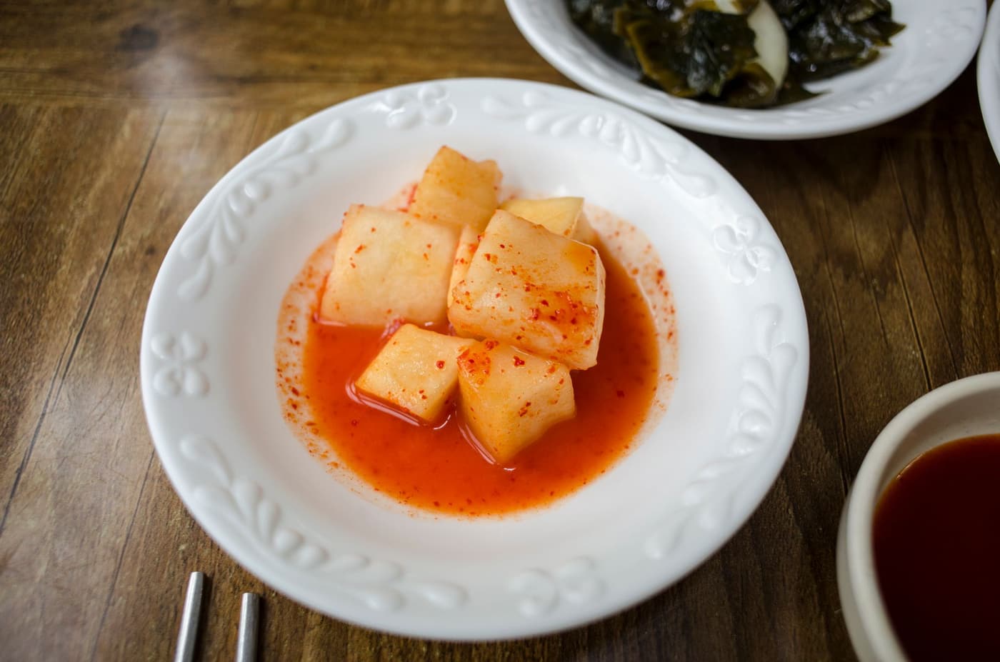 Korean radish kimchi in a white dish, coated in red chili seasoning.
