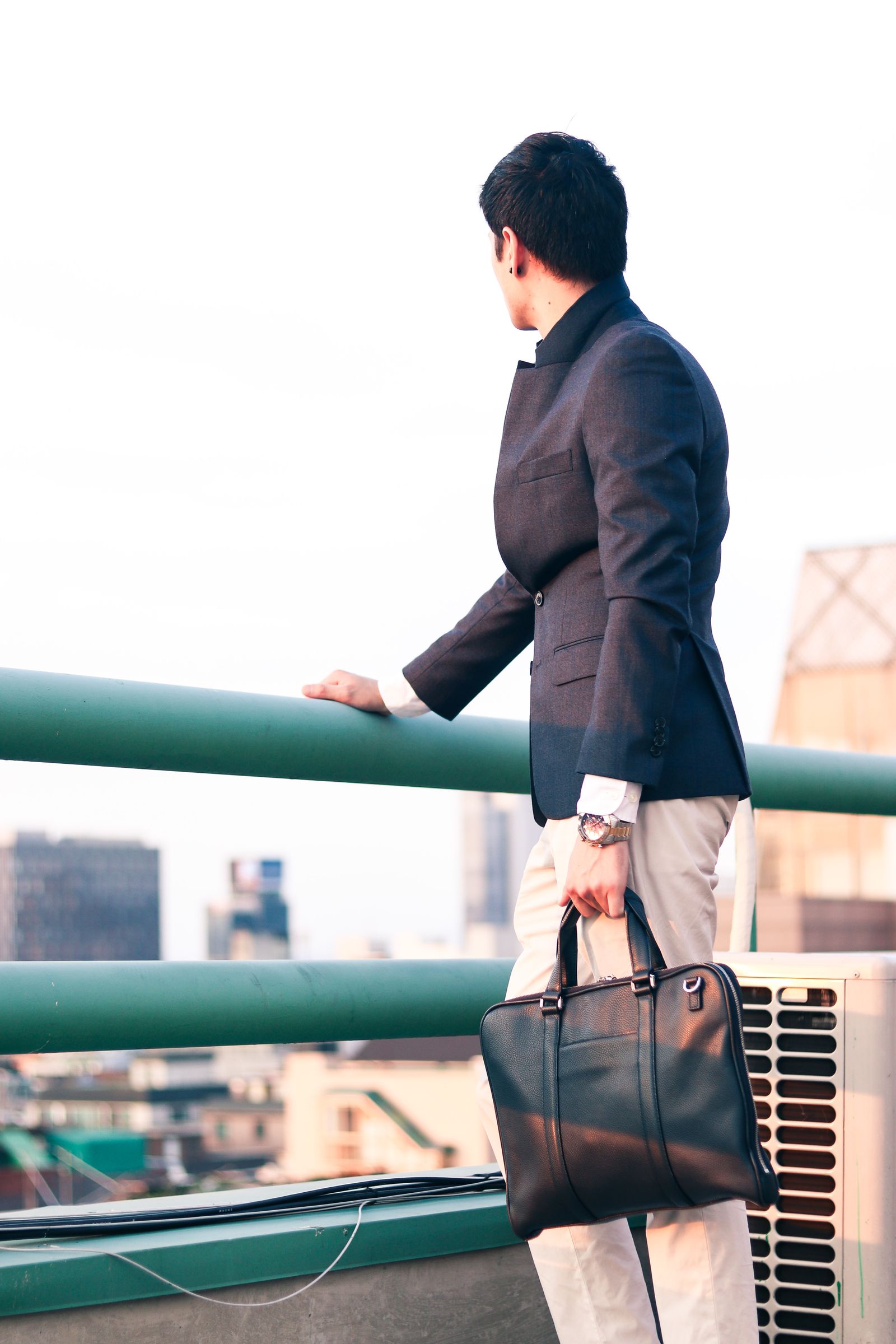 A young office worker in a suit stands on a Seoul rooftop, looking out over the city skyline.