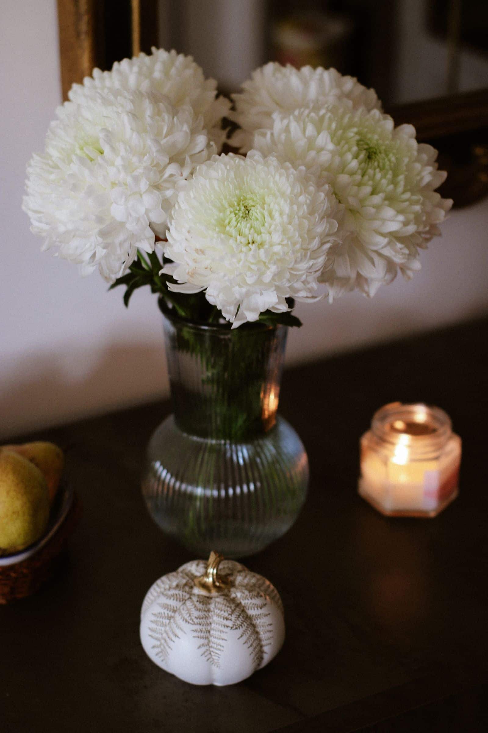 White chrysanthemums beside candlelight, a still life associated with memorial occasions.
