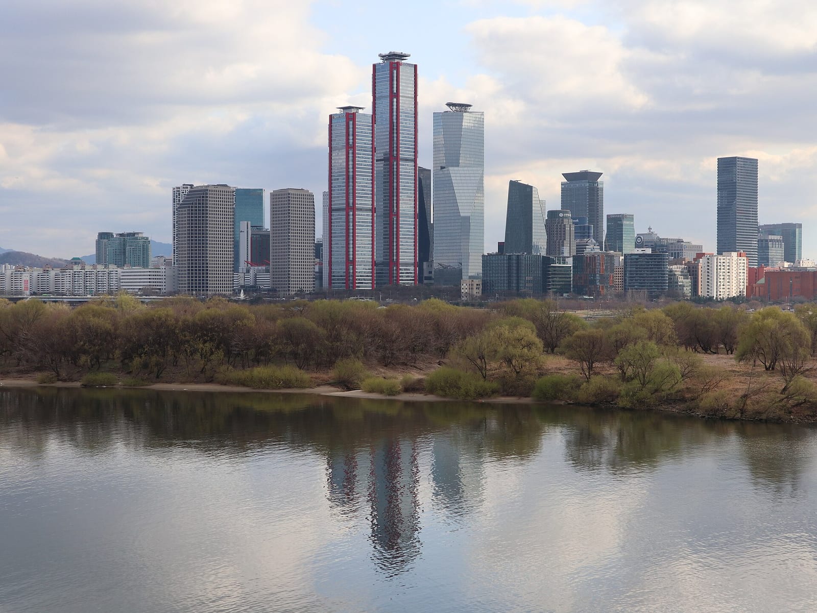 Wide river-level view of the Yeouido financial district skyline across the Han River, showing the Parc.1 twin towers and the Three IFC/IFC Mall tower cluster.