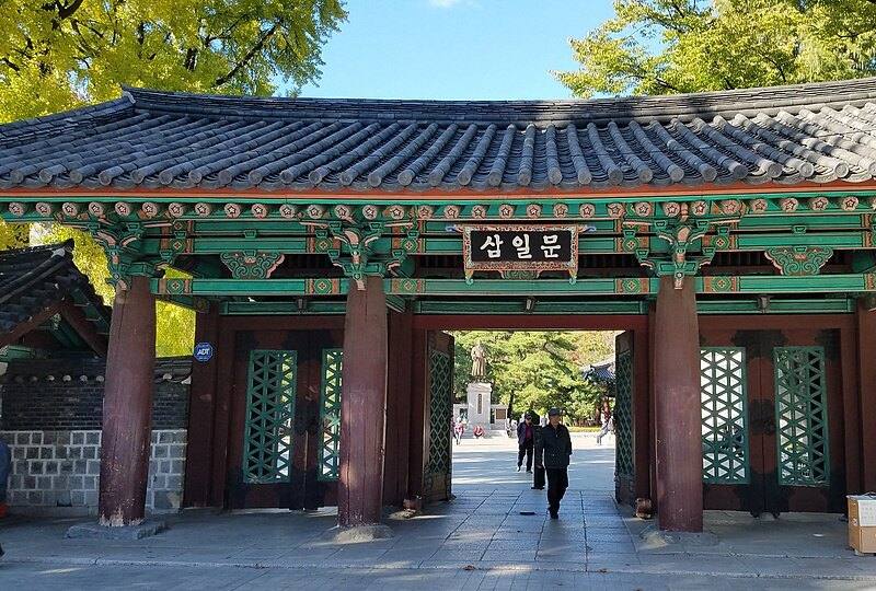 The Samilmun gate of Tapgol Park in Seoul: a traditional wooden gate with a tiled roof and green-painted eaves, the name board 삼일문, and autumn ginkgo trees behind.