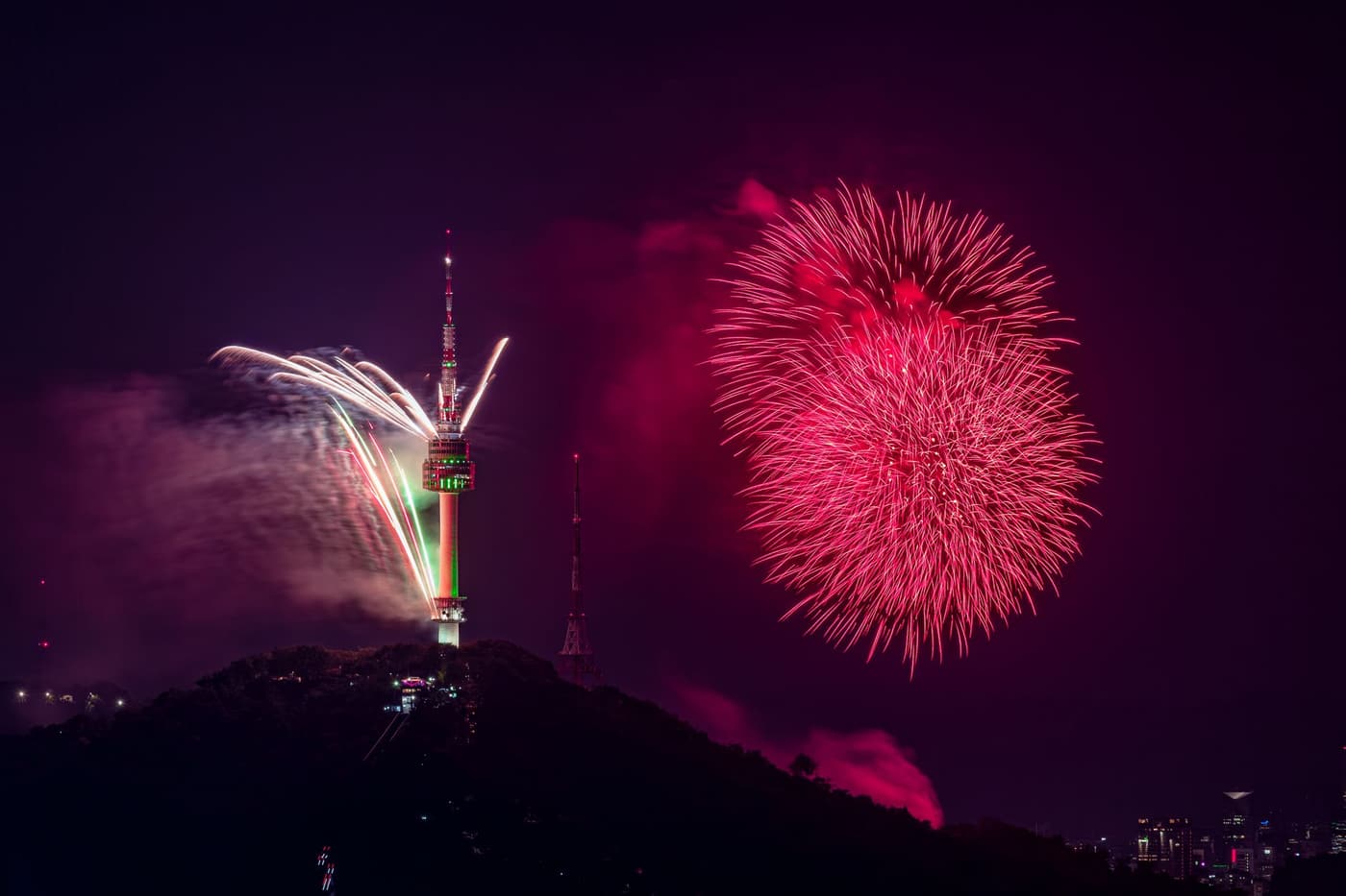 N Seoul Tower on Namsan at night with fireworks bursting beside it.