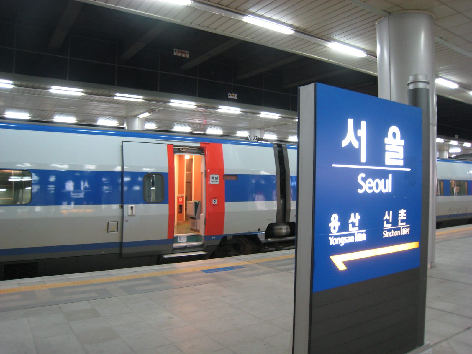 A KTX high-speed train at a platform, with an overhead station sign visible.