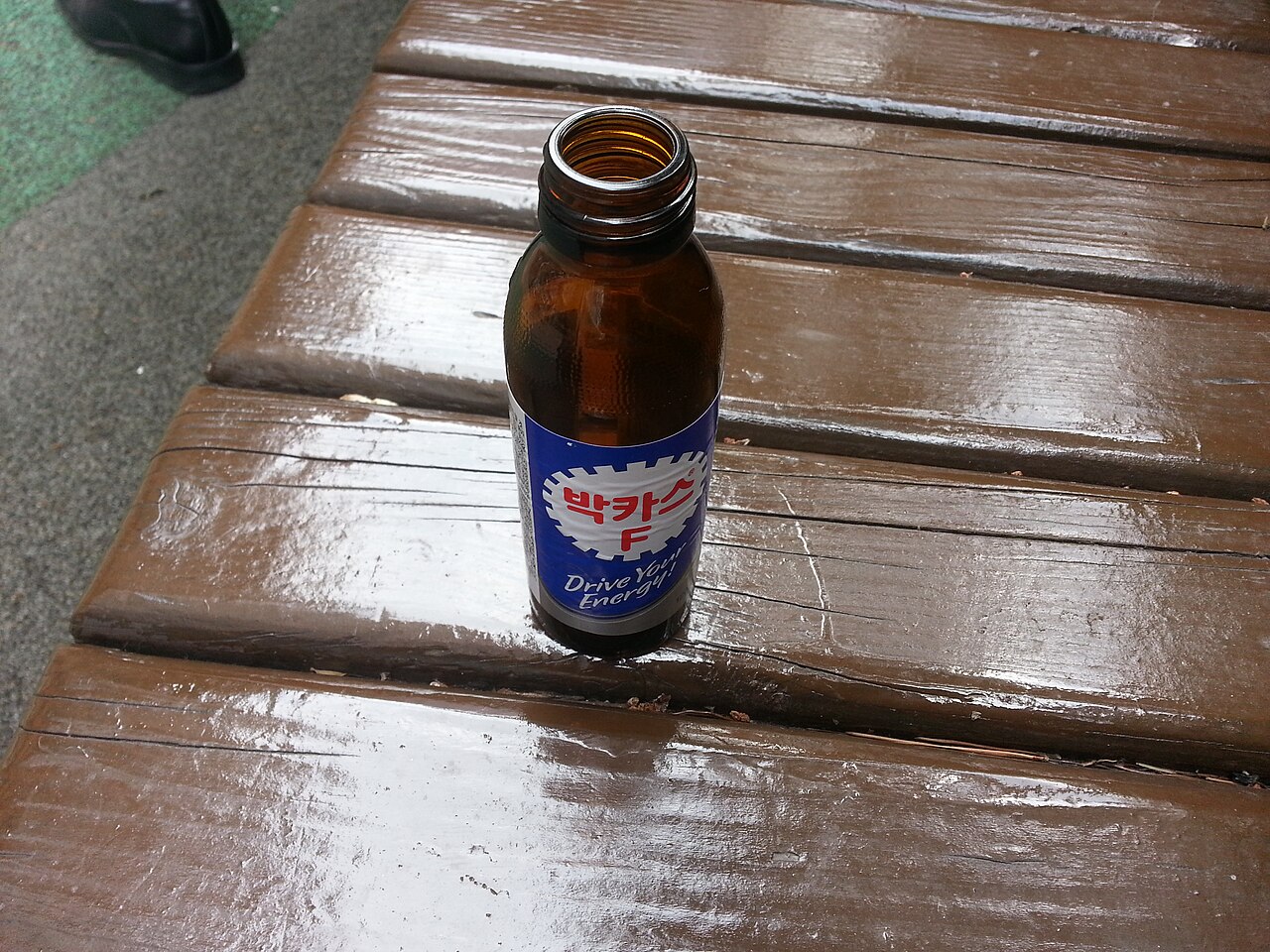 A Bacchus F bottle standing on an outdoor wooden bench.