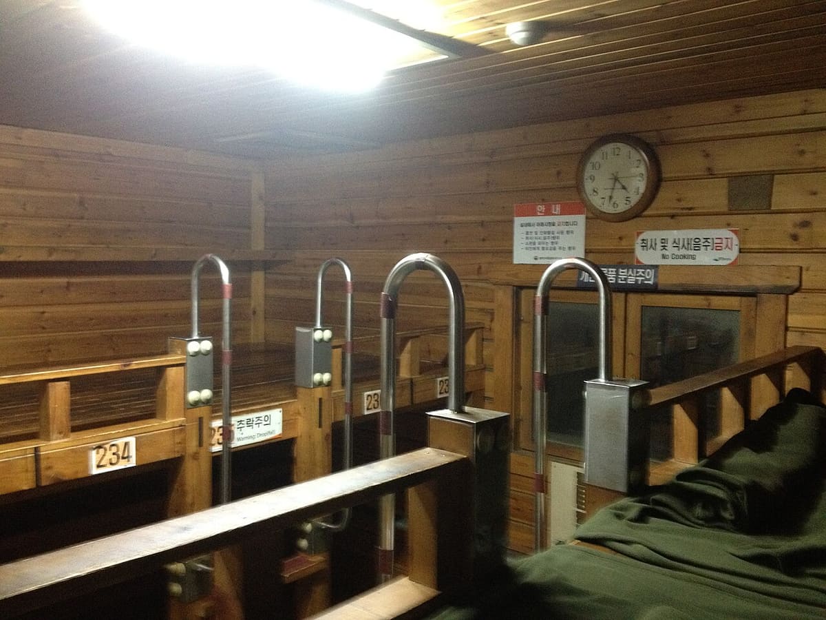 Inside Jungcheong Shelter: numbered wooden sleeping platforms and a wall sign reading No Cooking.